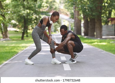 Sport Trauma. Young Black Woman Suffering From Acute Knee Pain During Jogging In Park, Caring Boyfriend Massaging Sore Place