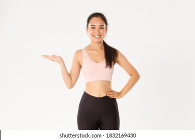 Sport, Wellbeing And Active Lifestyle Concept. Portrait Of Cheerful Attractive Asian Fitness Coach, Female Athlete Introduce Or Demonstrate Product For Workout, Holding Something On Hand