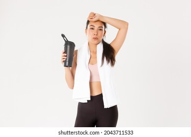 Sport, Wellbeing And Active Lifestyle Concept. Tired But Satisfied Asian Fitness Girl Wiping Sweat From Forehead And Exhale After Good Workout, Drinking Water Or Protein During Training Session