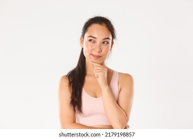 Sport, wellbeing and active lifestyle concept. Close-up of thoughtful asian fitness girl, female athlete making plan, looking cunning upper left corner while pondering, choosing something