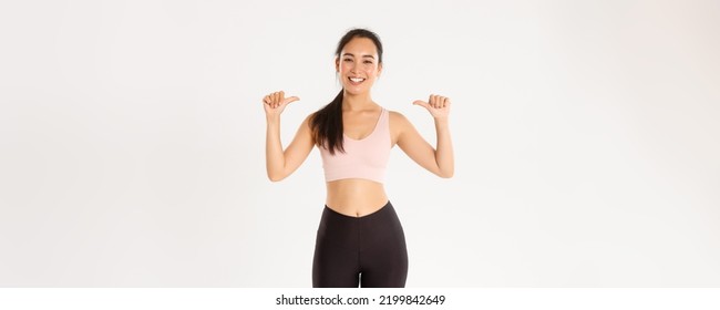 Sport, Wellbeing And Active Lifestyle Concept. Proud And Happy Smiling Asian Female Fitness Instructor, Sportswoman Pointing At Herself, Gaining Workout Goal, Become Gym Member, White Background