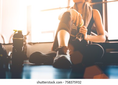Sport woman sitting and resting after workout or exercise in fitness gym with protein shake or drinking water on floor. Relax concept. Strength training and Body build up theme. Warm and cool tone 