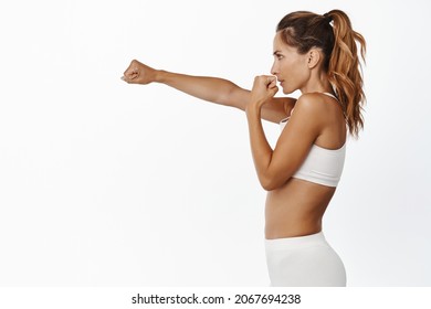 Sport and women health concept. Profile portrait of strong and fit middle aged woman stretching fist, punching air, shadowboxing and fighting, workout in gym - Powered by Shutterstock