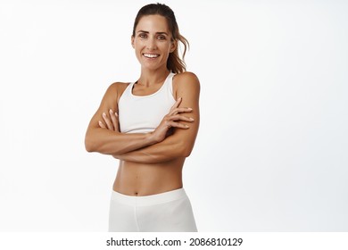 Sport And Women Health. Smiling Sportswoman With Abs And Muscles In Sportsbra, Cross Arms On Chest, Looking Confident At Camera, Workout Indoors, White Background