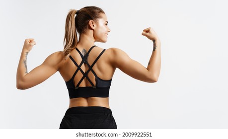 Sport and women. Rear view of strong fitness athlete, female bodybuilder, flexing muscles, showing fit body, biceps and athletic back, smiling satisfied, white background - Powered by Shutterstock