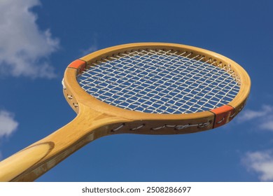 Sport wooden retro tennis racket on sky background outdoors. Wooden racket close up. - Powered by Shutterstock