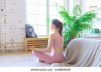 Sport young girl. Woman practicing yoga indoors at home. Girl sits near large window in Lotus position and meditates. Yoga asana, concept of health, Yoga in my heart