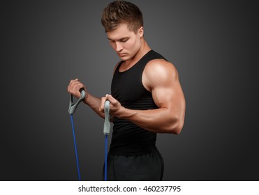 Sport. Young Man In Black Shirt Train His Biceps With Expander. Studio Black Background.