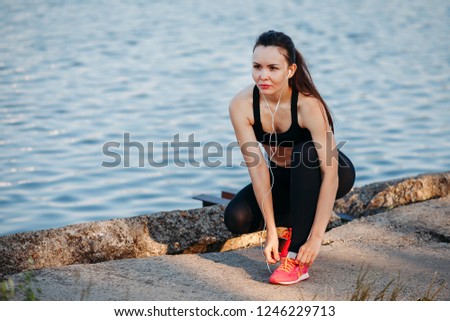 sport young woman tying shoelaces on pink sneakers. listens to music with headphones
