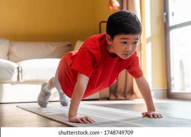 sportive asian kid doing push ups on fitness mat at home during self isolation - Powered by Shutterstock