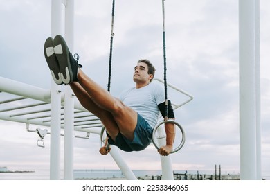 Sportive and athletic man does functional training exercise at the outdoor gym - Adult athlete doing workout at sunrise at calisthenics park on the beach - Fitness, healthy lifestyle and sport concept