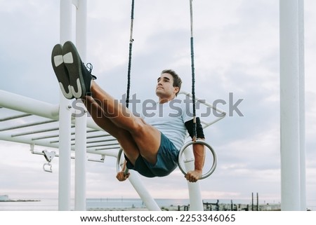 Sportive and athletic man does functional training exercise at the outdoor gym - Adult athlete doing workout at sunrise at calisthenics park on the beach - Fitness, healthy lifestyle and sport concept