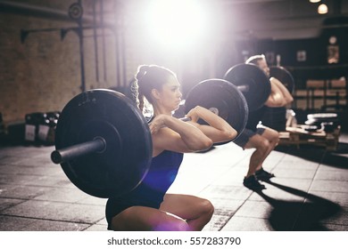 Sportive Athletic Man And Woman Lifting Heavy Barbells On Shoulders In Light Spacious Gym.