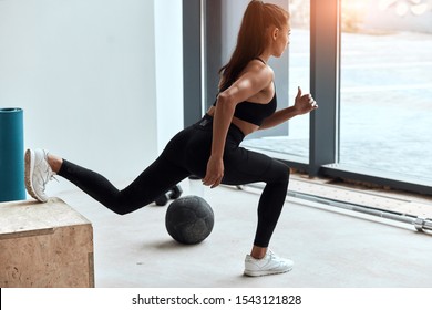 Sportive Female In Gym Doing Squats, Stretching Legs. One Leg On Fit Box. Side View On Perfect Woman's Body