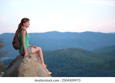 Sportive female hiker sitting alone taking a break on hillside trail. Lonely woman enjoying view of summer nature from rocky cliff on wilderness path. Active lifestyle concept - Powered by Shutterstock