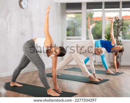 Sportive focused sports women standing in Parivrtta Trikonasana or Revolved Triangle Pose on mats during group yoga training in fitness center