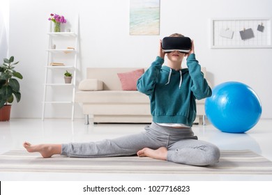sportive girl stretching with virtual reality headset on yoga mat at home