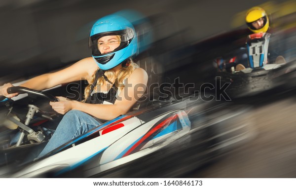 sportive happy woman in helmet driving\
car for karting with other people in sport club\
indoor