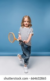 Sportive Little Girl Standing And Holding Tennis Raquet While Looking At Camera