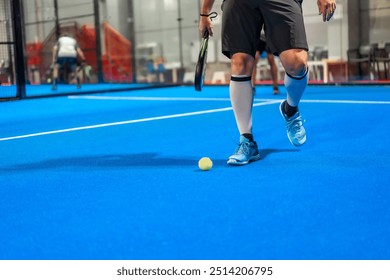 Sportive mature man picking up a paddle ball from the ground in an indoor blue court - Powered by Shutterstock