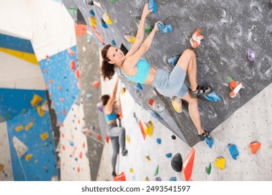 Sportive middle-aged woman climbing on artificial rock wall in rock-climbing gym - Powered by Shutterstock