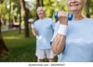 Sportive senior woman with sweatband does exercises with dumbbell training with friend in park