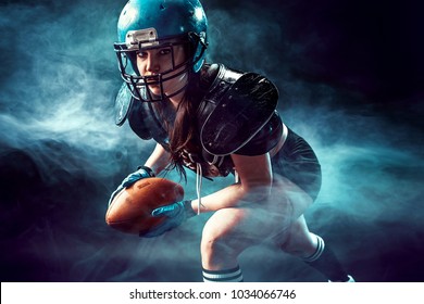 Sportive serious woman in helmet of rugby player holding ball in smoke.