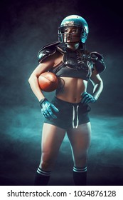 Sportive serious woman in helmet of rugby player holding ball in stuio on dark background. Side view, smoke