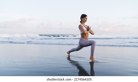 Sportive woman dressed in casual tracksuit doing yoga practice during weekend time at coastline beach, athletic female checking body flexibility while exercising at seashore during leisure on nature - Powered by Shutterstock