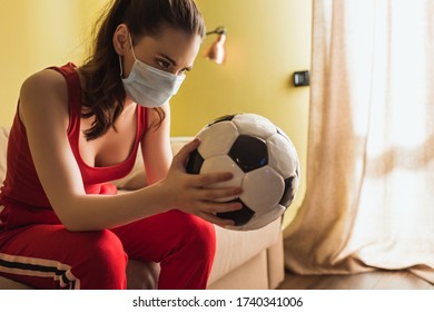 Sportive Woman In Medical Mask Looking At Football In Living Room
