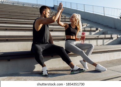 Sportive young couple, sitting on stairs outdoors and giving each other high five, fitness people after successful workout - Powered by Shutterstock