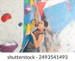 Sportive young girl climbing on artificial rock wall in rock-climbing gym