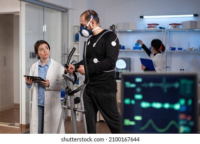 Sportman with medical electrodes on it running on fitness trainer working at body endurance during medical workout in modern laboratory while doctor monitoring EGK data. Heart rate pulse on monitor - Powered by Shutterstock