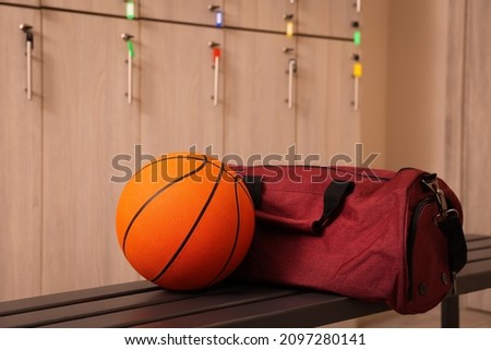 Sports bag and basketball ball on wooden bench in locker room