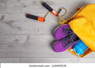 Sports bag with gym equipment on wooden background, top view