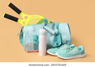 Sports bag with sportswear, tennis rackets and bottle of water on beige background - Powered by Shutterstock