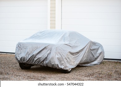 Sports car under silver colored cover outside a closed garage.