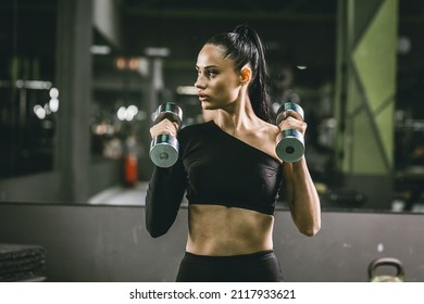 Sports career of a young Athlete. Strong life position. Portrait of an athlete with dumbbells on the background of the sports hall.