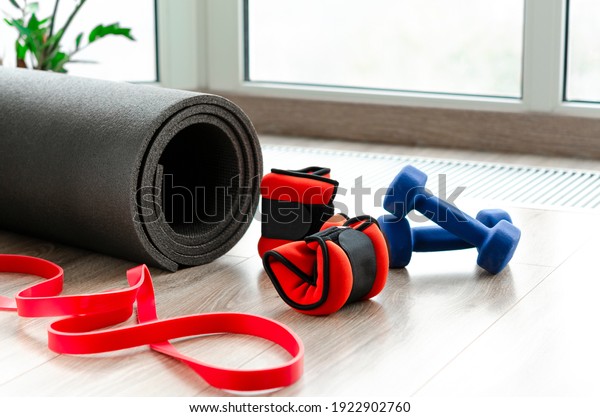 Sports\
concept. Fitness kit at home. Fitness mat, weights for arms and\
legs, dumbbells and harness lie on the\
floor