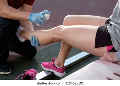 Sports Doctor Treating Injured Sportman's Knee. Sport Medicine In Action. Injured Tenis Player's Or Athlete Leg Is Anesthetizing By Sport Doctor Using Freezing Spray.