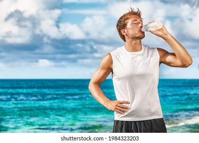 Sports Drink Fitness Man Drinking Water Botlle During Outdoor Exercise Workout On Beach. Dehydrated Athlete Runner After Run Sweating In Summer Heat Exercising Cardio.