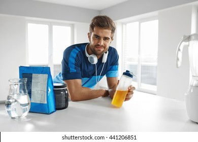 Sports Energy Drink. Handsome Healthy Happy Man With Fit Muscular Body In Sportswear, Headphones With BCAA Amino Acid Beverage And Bodybuilding Nutrition Supplements In Kitchen Before Fitness Workout