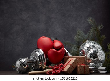 Sports Equipment: Dumbbell, Boxing Gloves, Skipping Rope, Fir Branch, Christmas Ornament, Gifts On Dark Grey Background With Copy Space. Fitness, Sport, Healthy Lifestyle Concept. New Year. Christmas