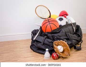 Sports Equipment In A Holdall Sports Bag On A Gym Floor. Football, Rugby, Baseball, Cricket, Basketball, Boxing, Badminton, Squash. With Copy Space.