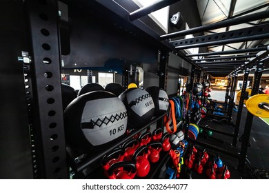 Sports Equipment In Various Colors In A Modern Gym Concept. Equipments Are Stacked On A Metal Shelf - Bars, Medicine Balls, Dumbbells, Kettle Balls, Weights, Elastic Bands