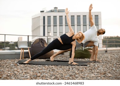 Sports family, husband and wife standing in yoga pose on mats with arms raised up against urban background. Happy couple doing sports at sunrise on the roof of a modern building. - Powered by Shutterstock