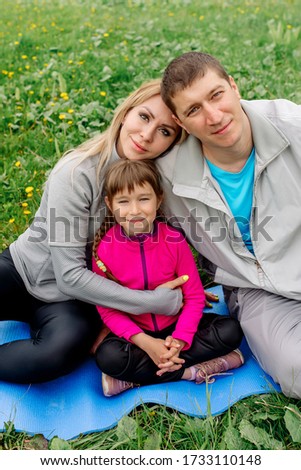 Sports family - mom, dad and daughter are sitting on the rug on the green lawn