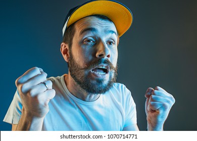 Sports, Fan Human Emotions And People Concept - Sad Young Man Watching Sports On Tv And Supporting Team At Home. Crying Emotional Man Screaming In Colorful Bright Lights At Studio. Facial Expression