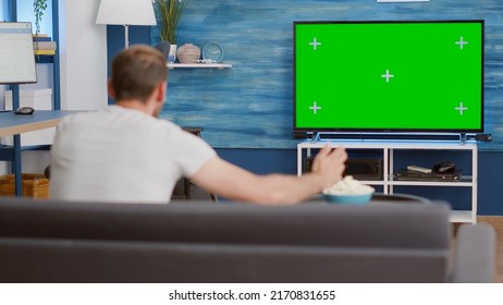 Sports Fan Watching Game On Green Screen Tv Mockup Encouraging Favourite Team While Relaxing At Home Sitting On Couch. Man Sport Supporter Looking At Television With Chroma Key Display In Living Room.