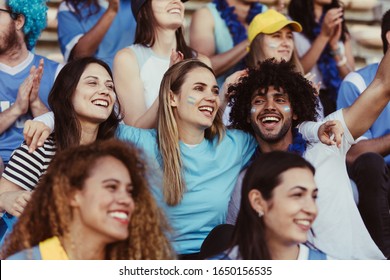 Sports Fans In Crowd Having Fun Watching A Game At Stadium. Happy Argentinian Soccer Fans Watching A Live Match In Stadium.